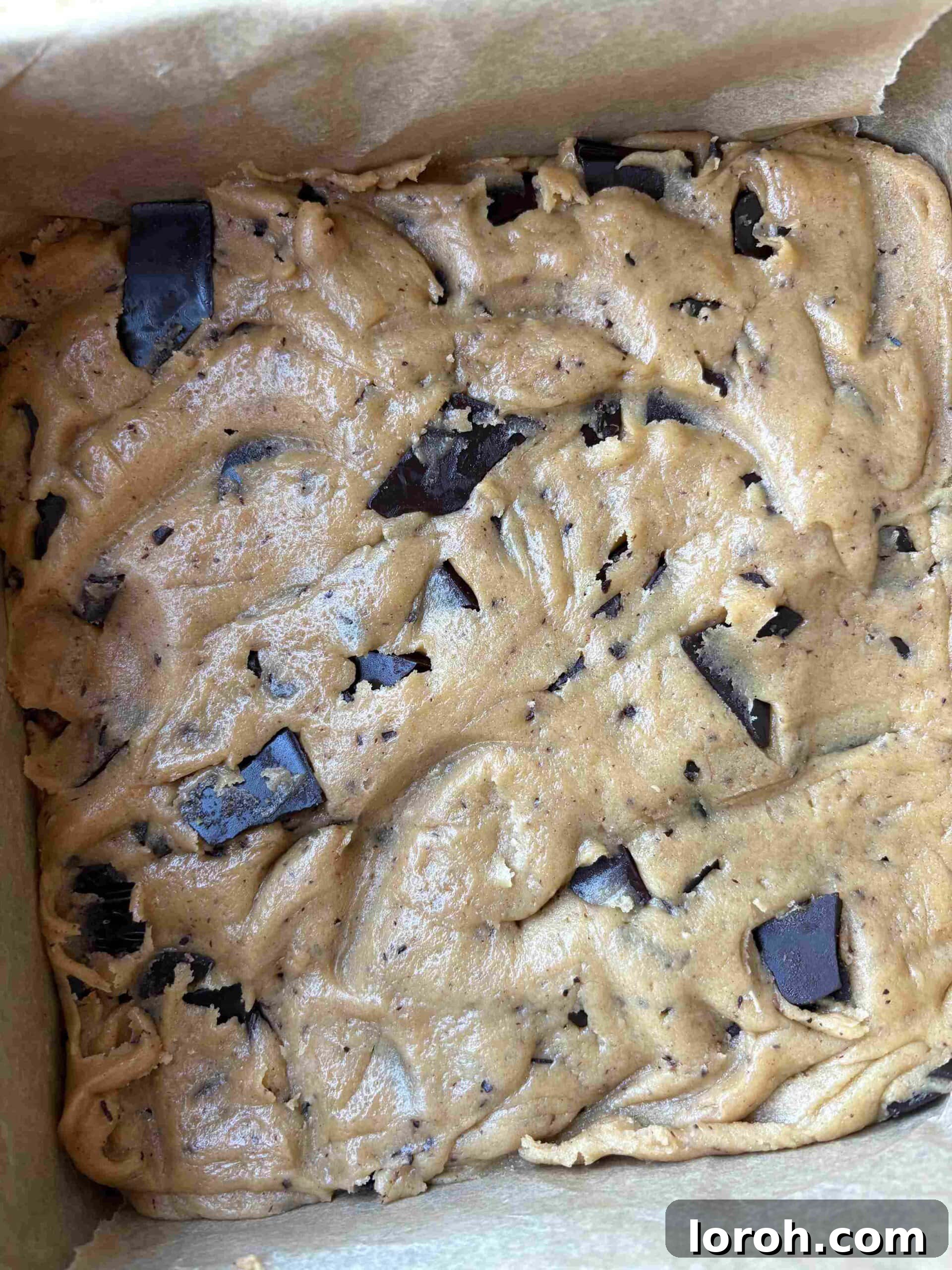 Ultimate Chocolate Chip Cookie Bars 14 Pressing chocolate chip cookie bar dough into a lined baking tin, topped with extra chocolate and flaky salt.