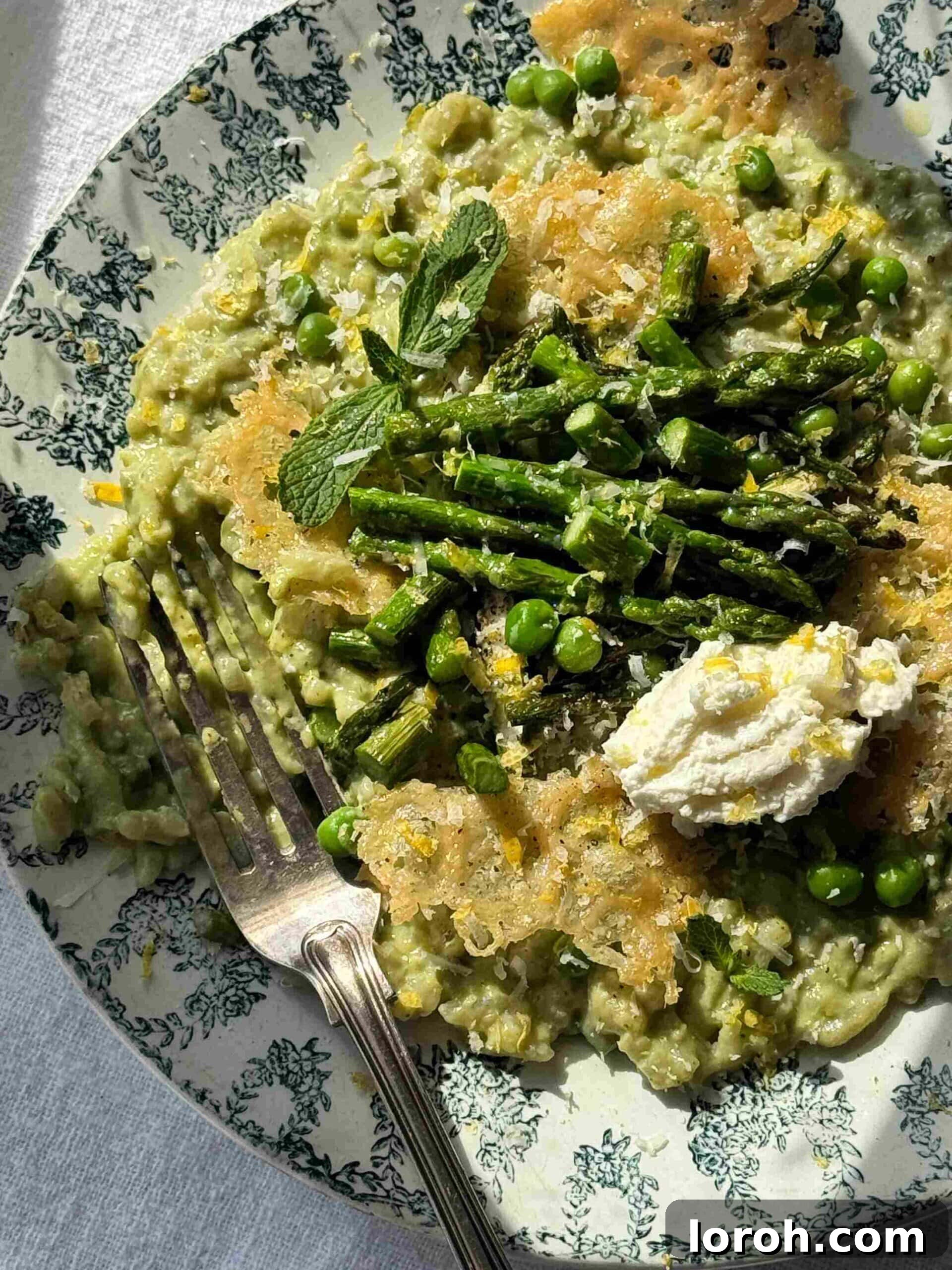 Vibrant Spring Asparagus Risotto 2 A beautifully plated creamy asparagus and pea risotto, garnished with whole roasted asparagus spears and a dollop of mascarpone, served on a blue ceramic plate.