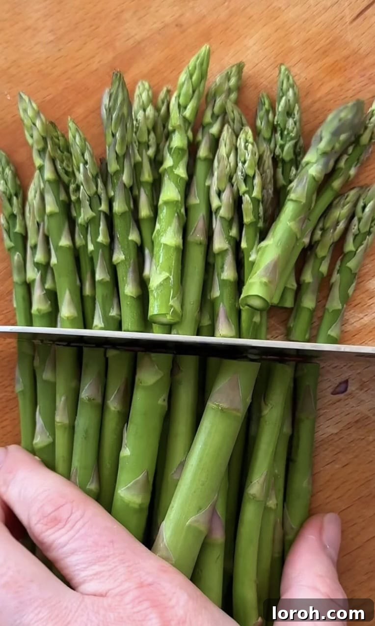 Vibrant Spring Asparagus Risotto 4 A hand demonstrating how to snap off the woody ends of asparagus spears and then slice the tips.