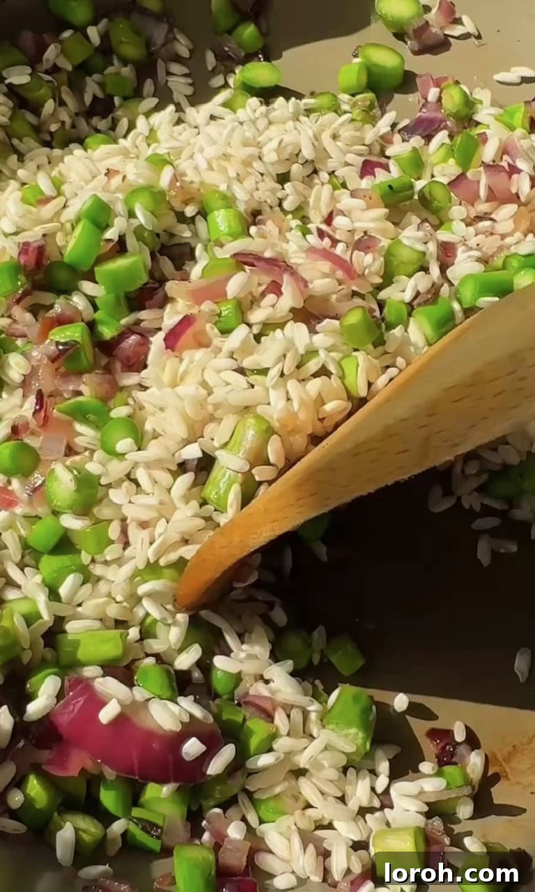 Vibrant Spring Asparagus Risotto 7 Adding sliced asparagus stalks and crushed garlic to the pan with softened onions before stirring in risotto rice.