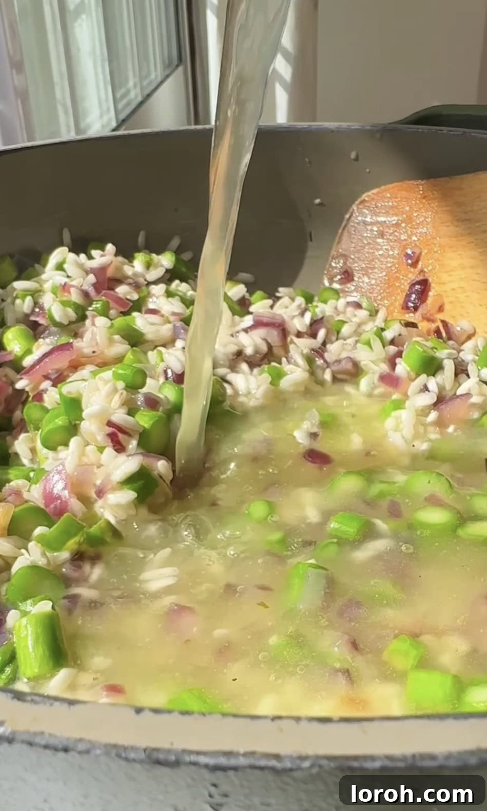 Vibrant Spring Asparagus Risotto 8 A ladle of hot stock being added to the risotto rice in a pan, with continuous stirring.