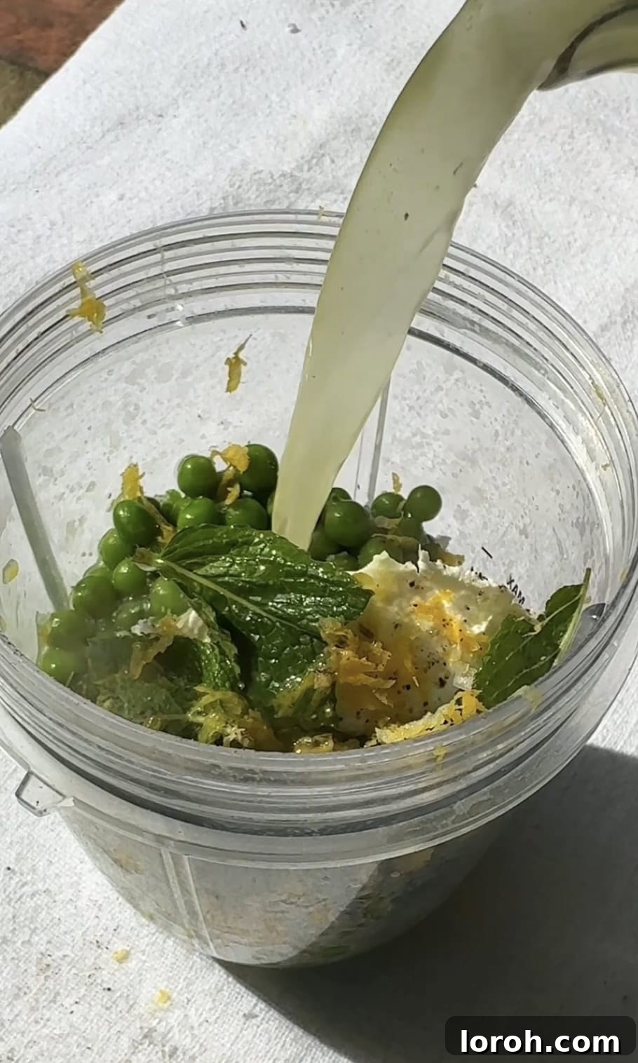 Vibrant Spring Asparagus Risotto 9 Frozen peas being blended with chicken stock, mascarpone, lemon juice, and mint leaves in a blender.