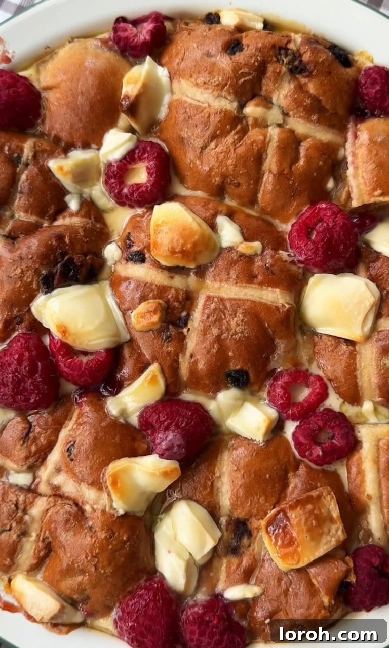 Image showing the hot cross bun bread and butter pudding freshly baked with a golden top, melted white chocolate, and raspberries.