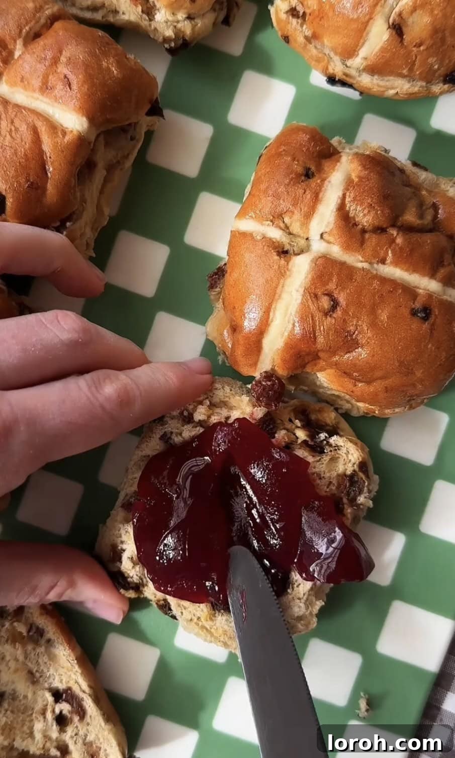 Image showing raspberry jam being spread generously on a hot cross bun half.
