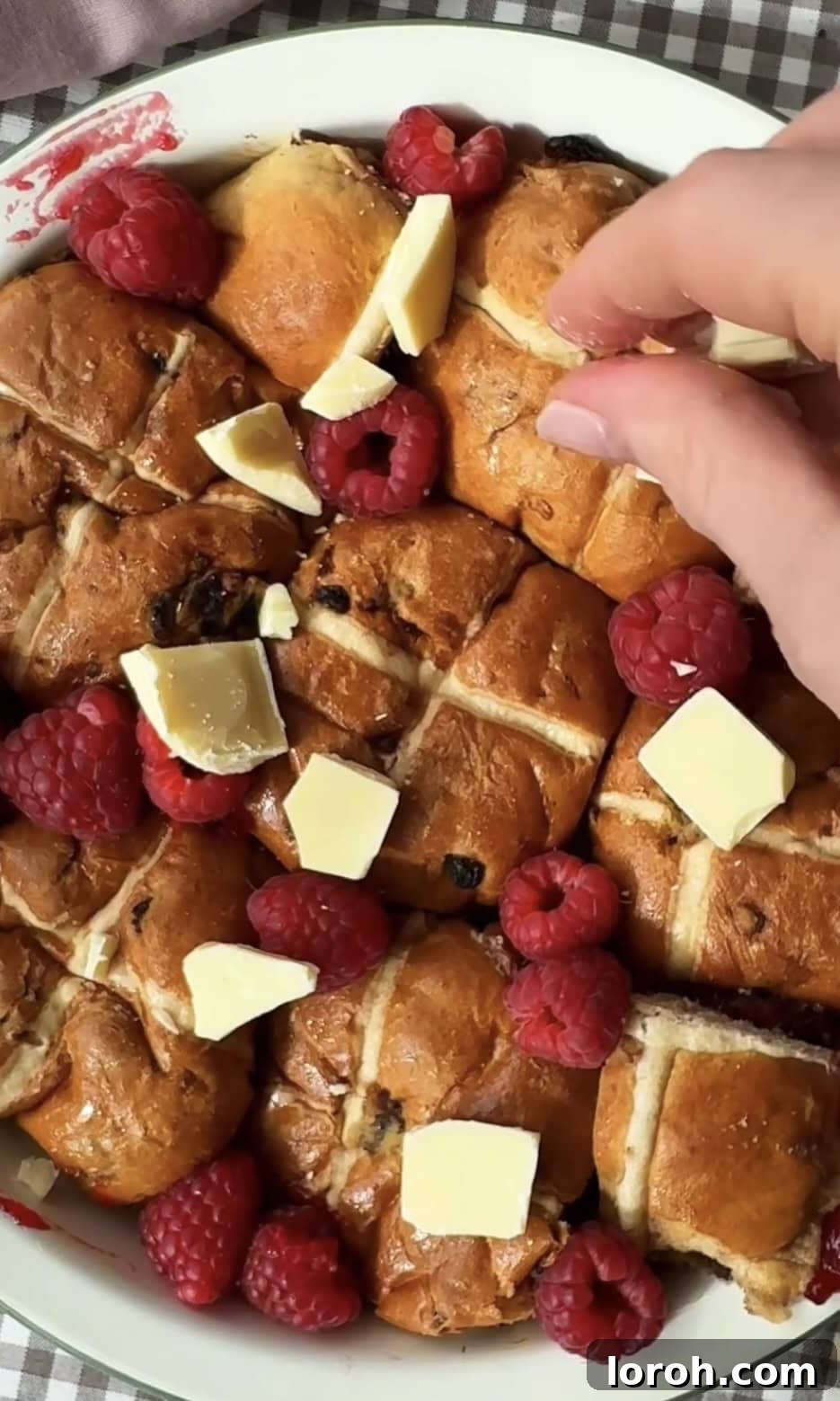 Image showing the remaining raspberries and white chocolate being scattered over the arranged hot cross buns.