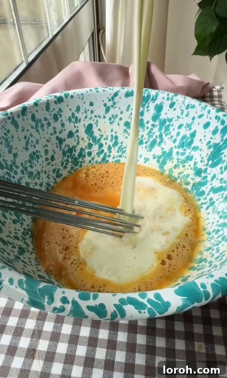 Image showing warm milk being gradually poured into the egg and sugar mixture while whisking to create the custard.