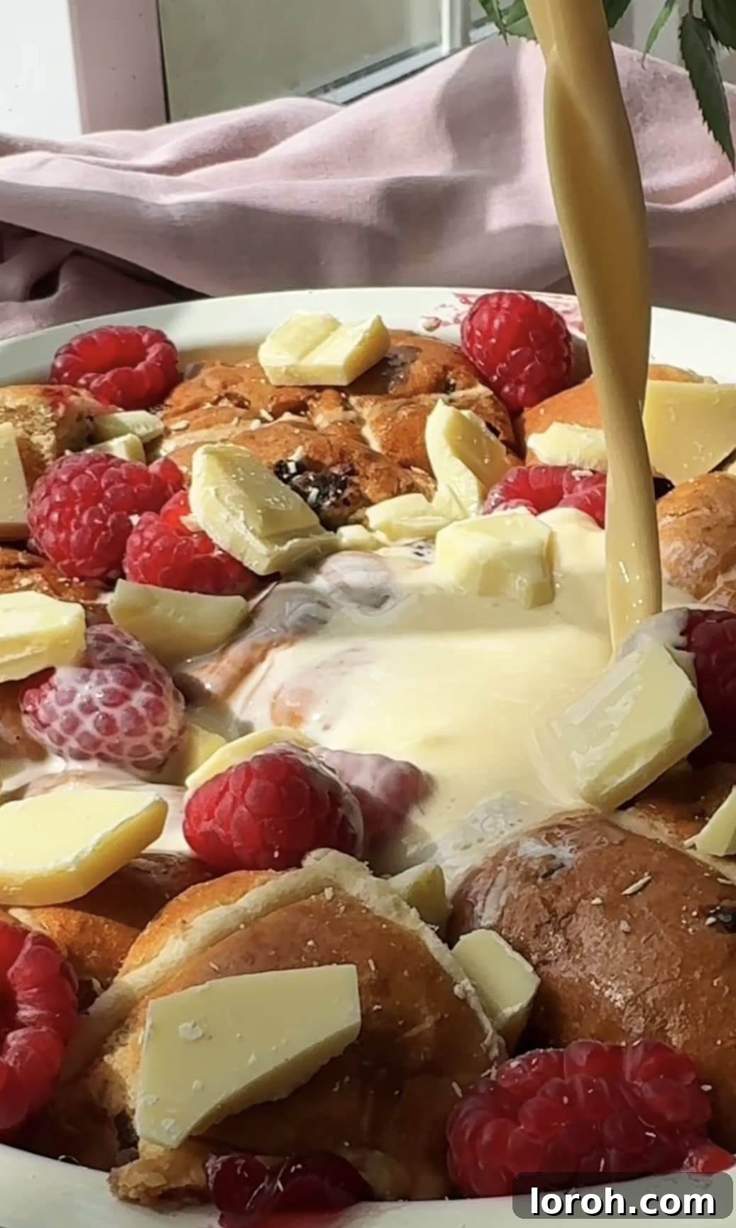 Image showing the prepared custard being poured evenly over the arranged hot cross buns in the baking dish.
