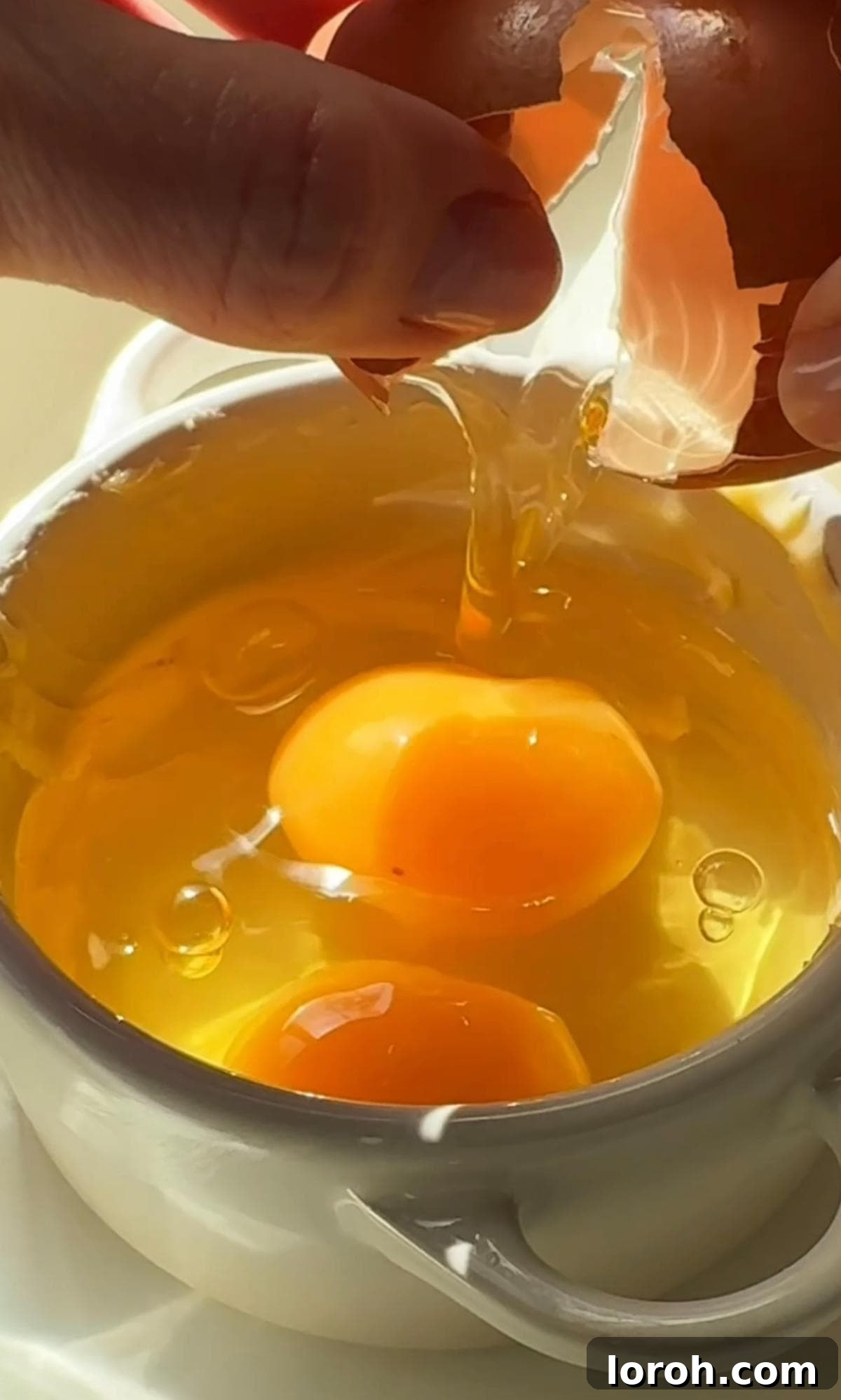 Cracking two fresh eggs directly into a buttered ramekin.