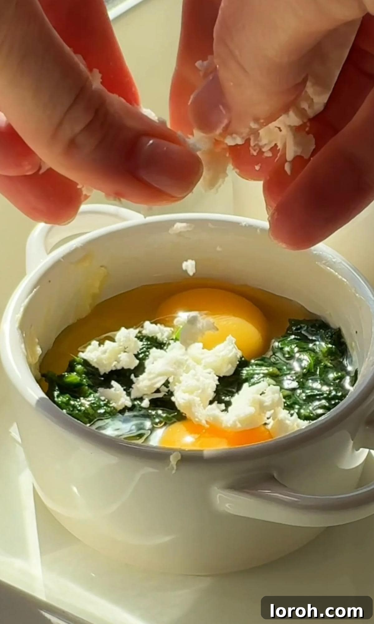 Adding crumbled feta cheese over the eggs and spinach in a ramekin.