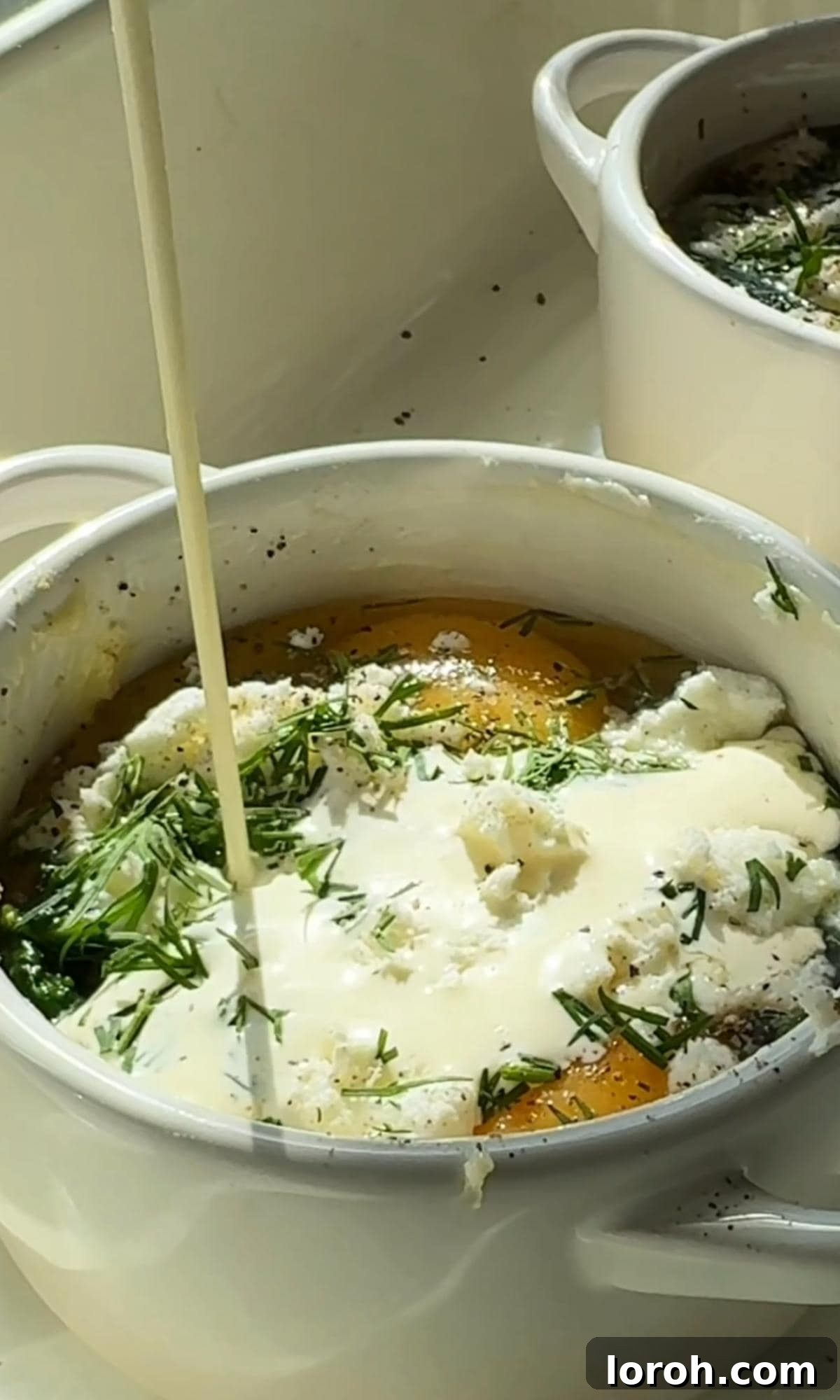 Pouring double cream over the eggs, feta, and spinach in a ramekin.