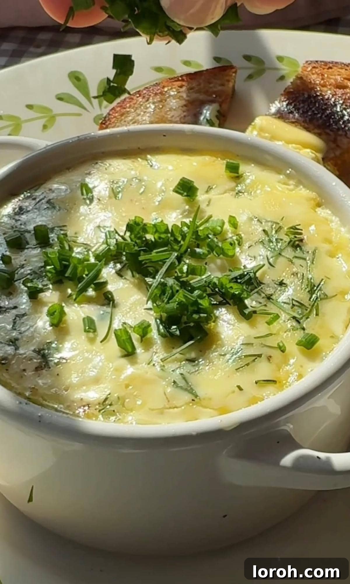Garnishing freshly baked Oeufs Cocotte with chopped chives before serving.