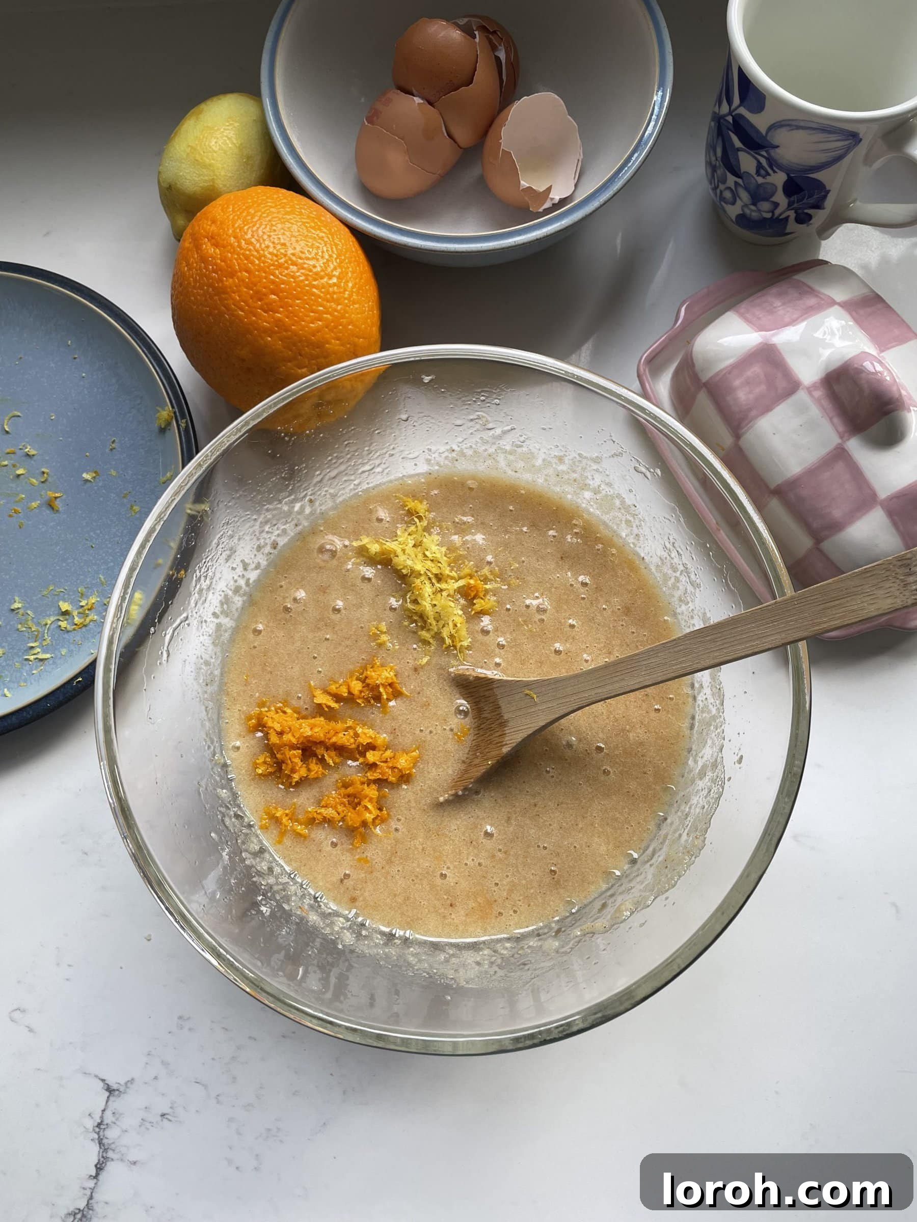 The vibrant addition of orange and lemon zest to the cake mix in a glass mixing bowl.