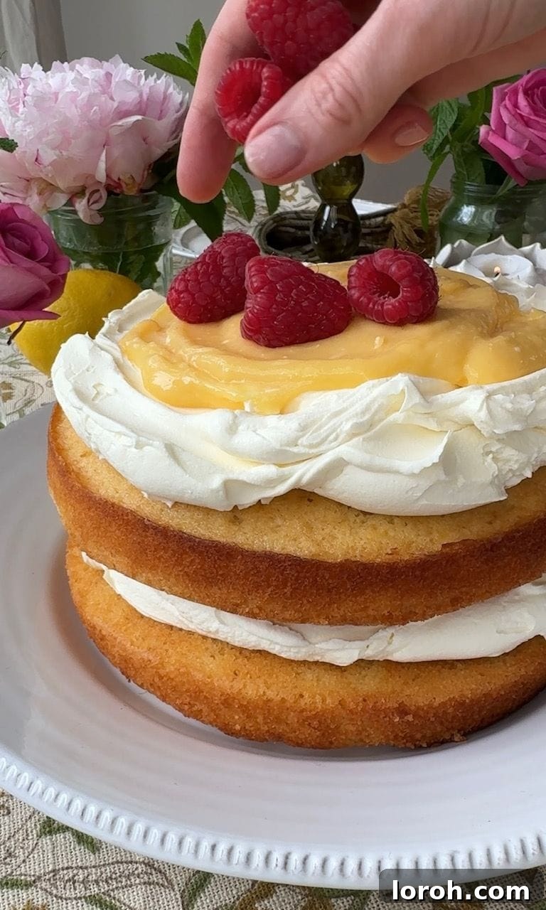 The fully assembled lemon curd cake topped with fresh raspberries and lemon slices, ready to be served.