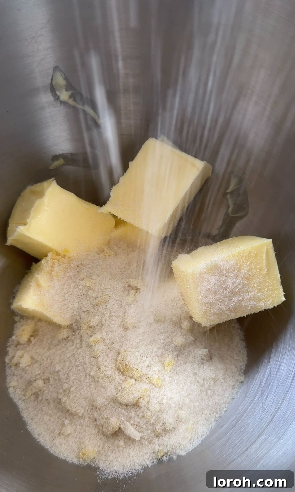 Softened butter being added to the lemon-infused sugar in a mixing bowl.