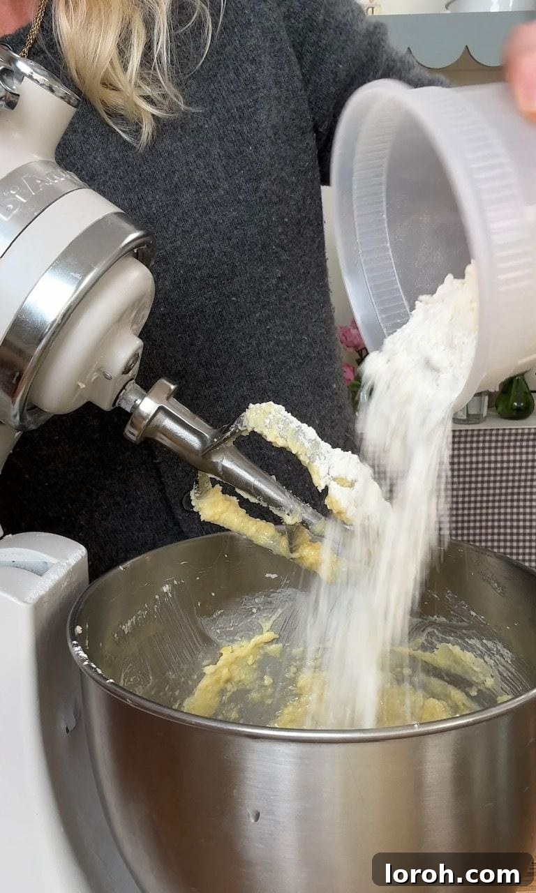 Plain flour and baking powder being gently tipped into the wet cake batter in a large mixing bowl.