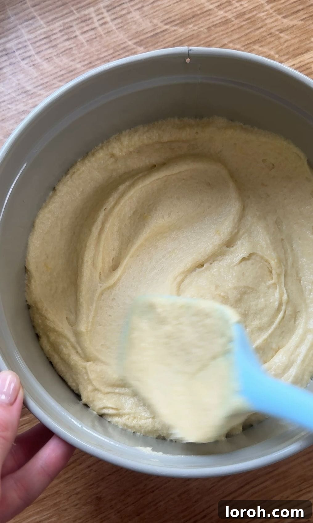 Smooth cake batter being spread evenly into a prepared round cake tin, ready for baking.