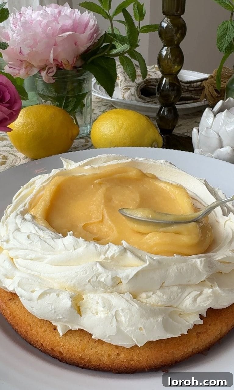 A generous layer of vibrant lemon curd being spread over a cooled cake sponge, ready for the next layer.