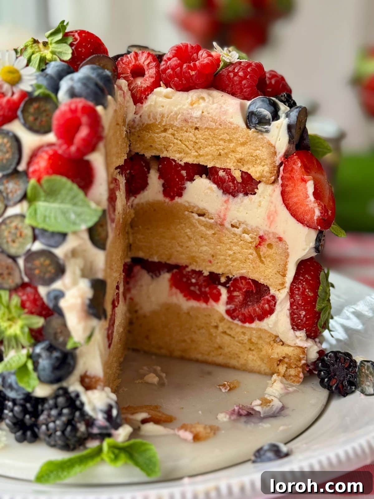 A beautiful slice of fresh berry cake showing layers of sponge, cream cheese frosting, and mixed berries.