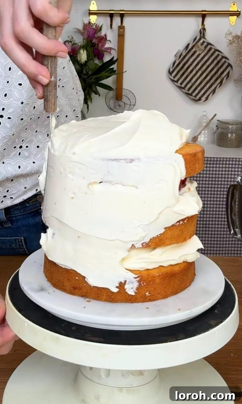 Smoothing cream cheese icing on the sides of a fresh berry cake.