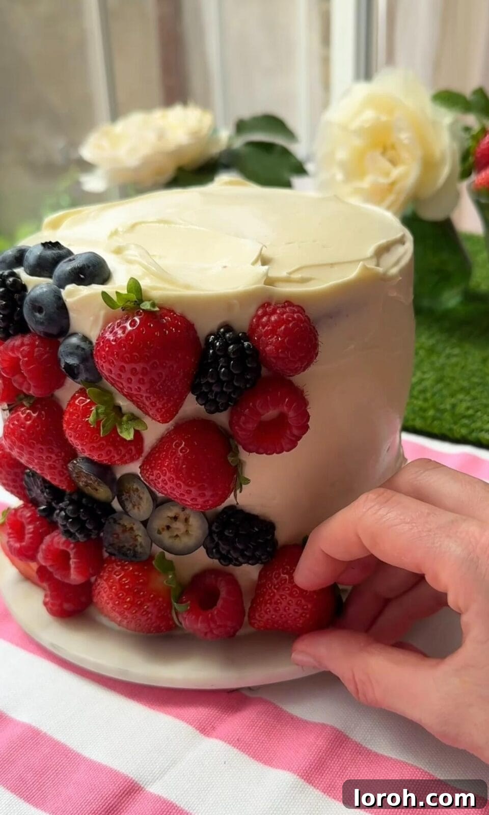 The final step: adding a generous assortment of fresh berries to the top of the frosted berry cake.