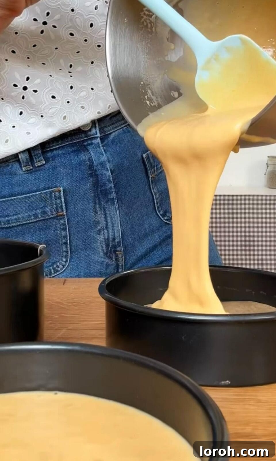 Separating cake batter evenly into three prepared cake tins.