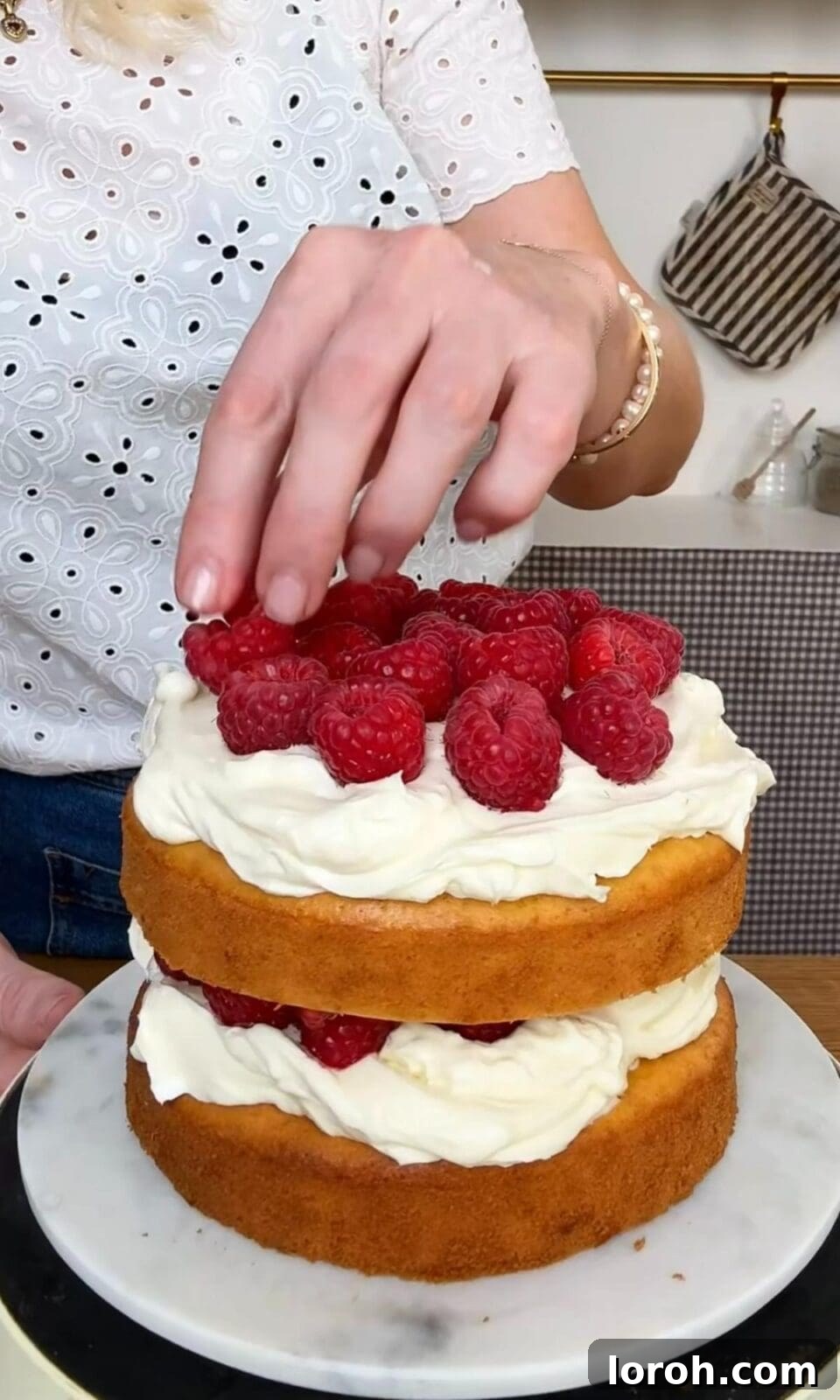 Adding a generous layer of fresh berries to the top of the berry cake's bottom layer.