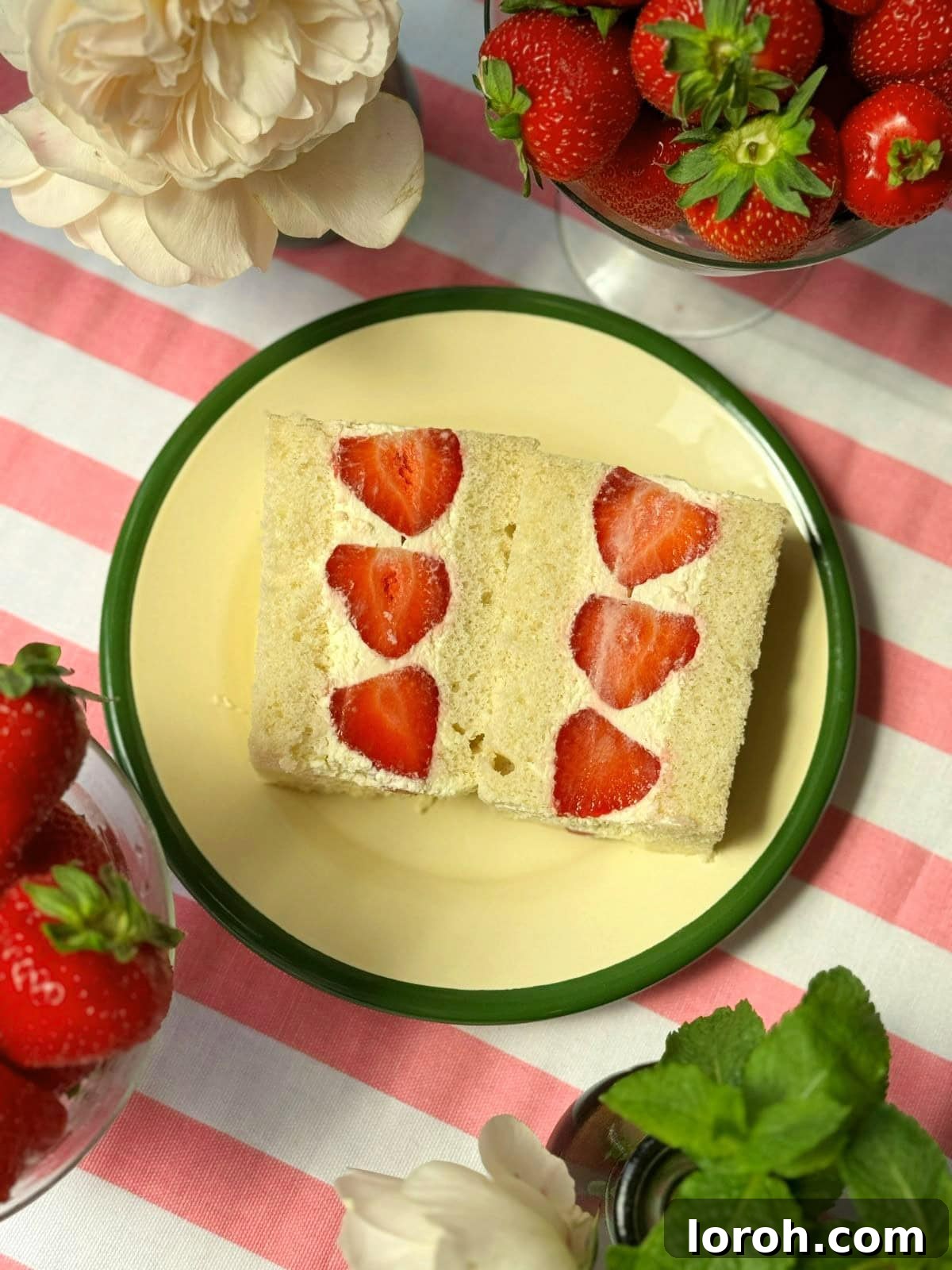 A vibrant Japanese strawberry sandwich (Ichigo Sando) with fresh strawberries and whipped cream, resting on a white plate with a green rim.