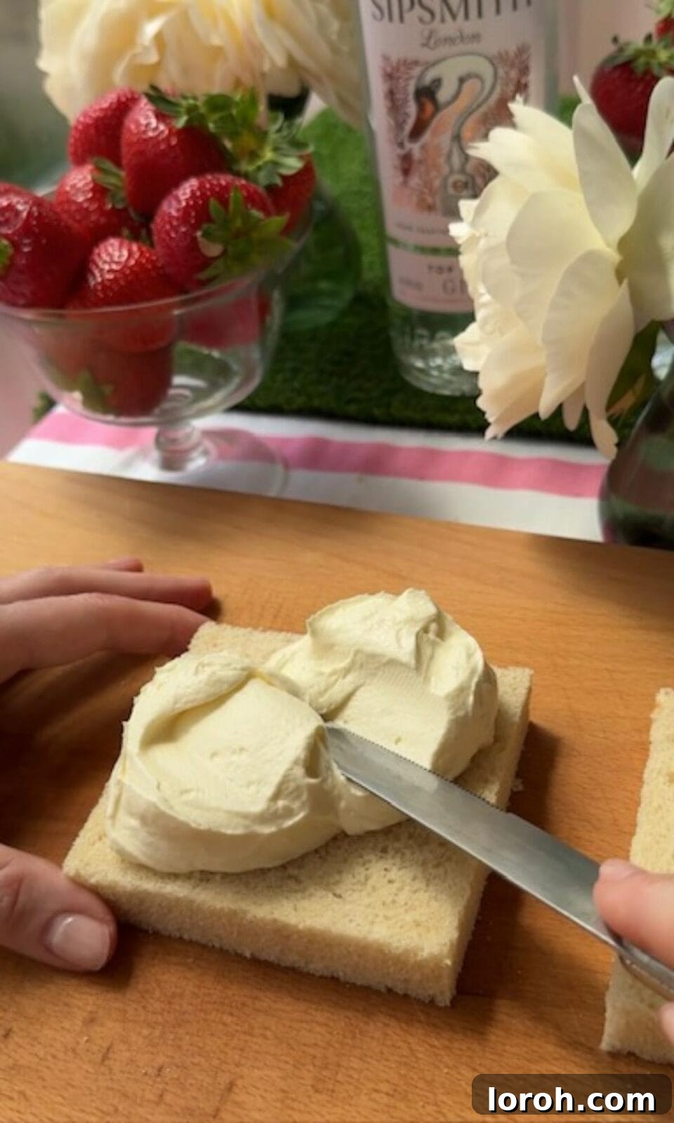 Spreading a generous layer of whipped cream onto a slice of Japanese milk bread for a strawberry sandwich.