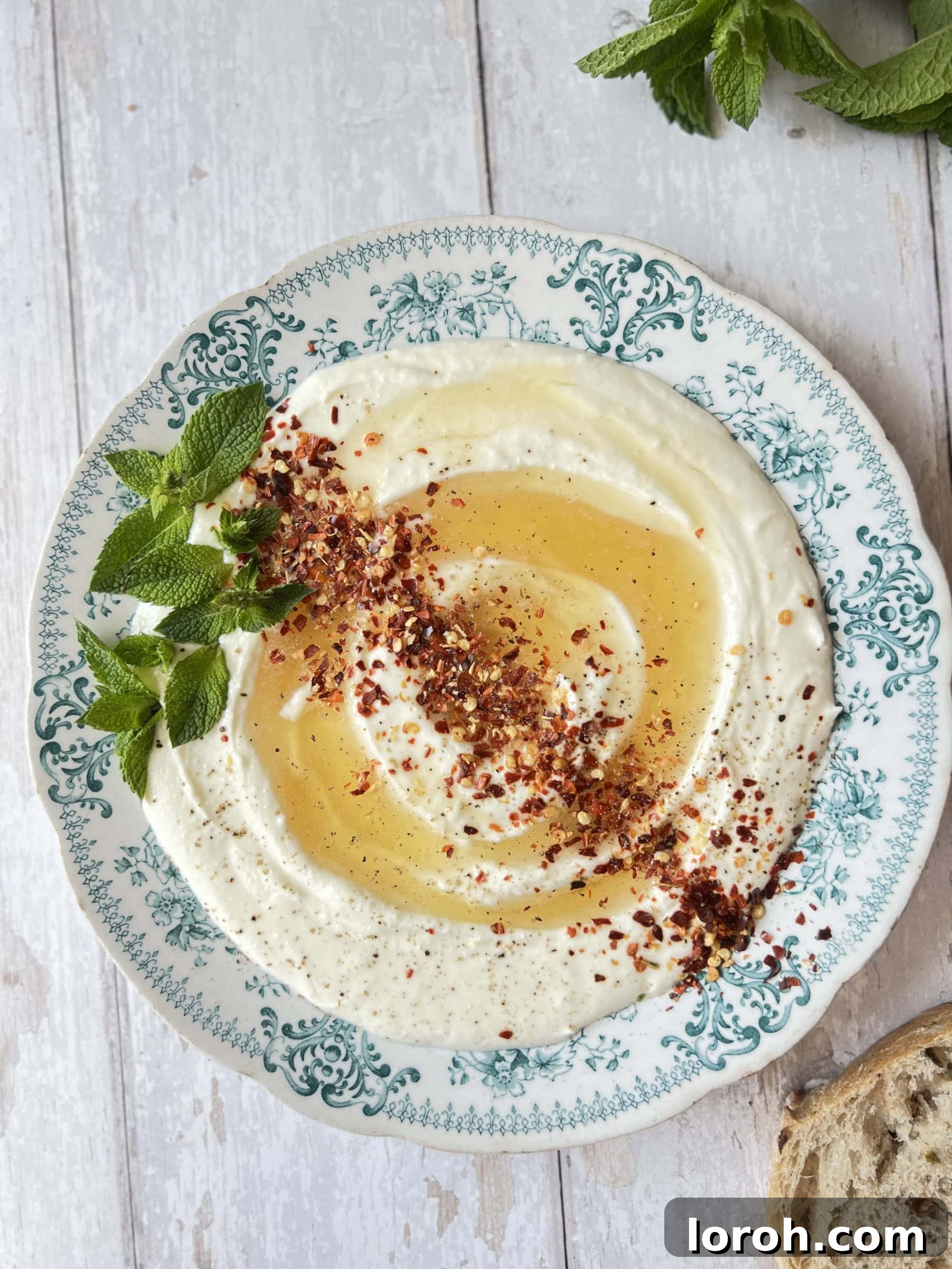 Creamy whipped ricotta cheese on a blue plate, garnished with a generous drizzle of hot honey and a sprinkle of chili flakes.