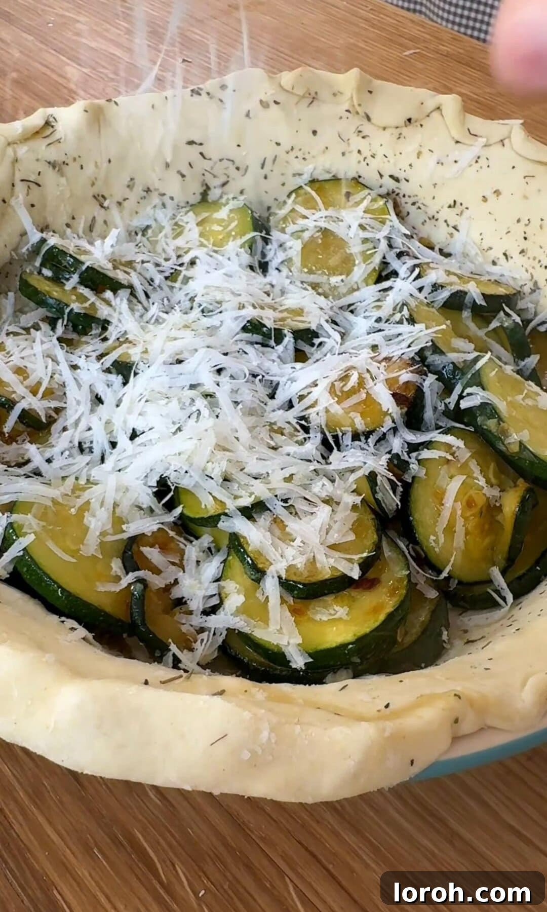 Spreading sautéed courgettes and grated Parmesan over the pastry base of the quiche.