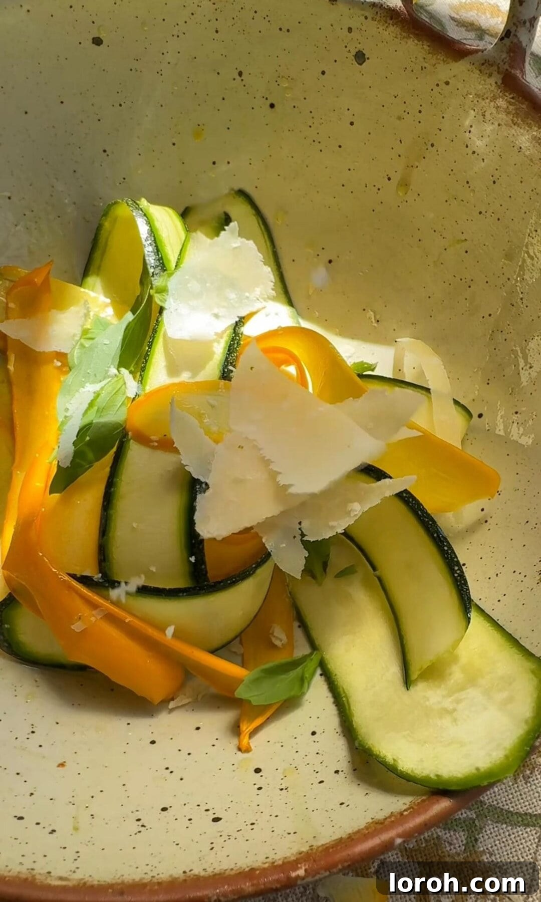 Tossing thinly shaved courgette ribbons with Parmesan, olive oil, salt, and pepper in a bowl.