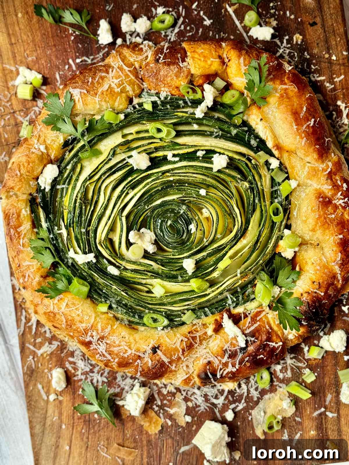 Golden Zucchini Feta Galette 2 Golden-baked Galette de Courgettes on a rustic wooden board, garnished with fresh herbs, ready to be served.