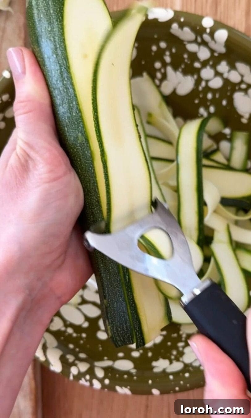 Golden Zucchini Feta Galette 6 A hand using a vegetable peeler to shave courgettes into long, thin ribbons.