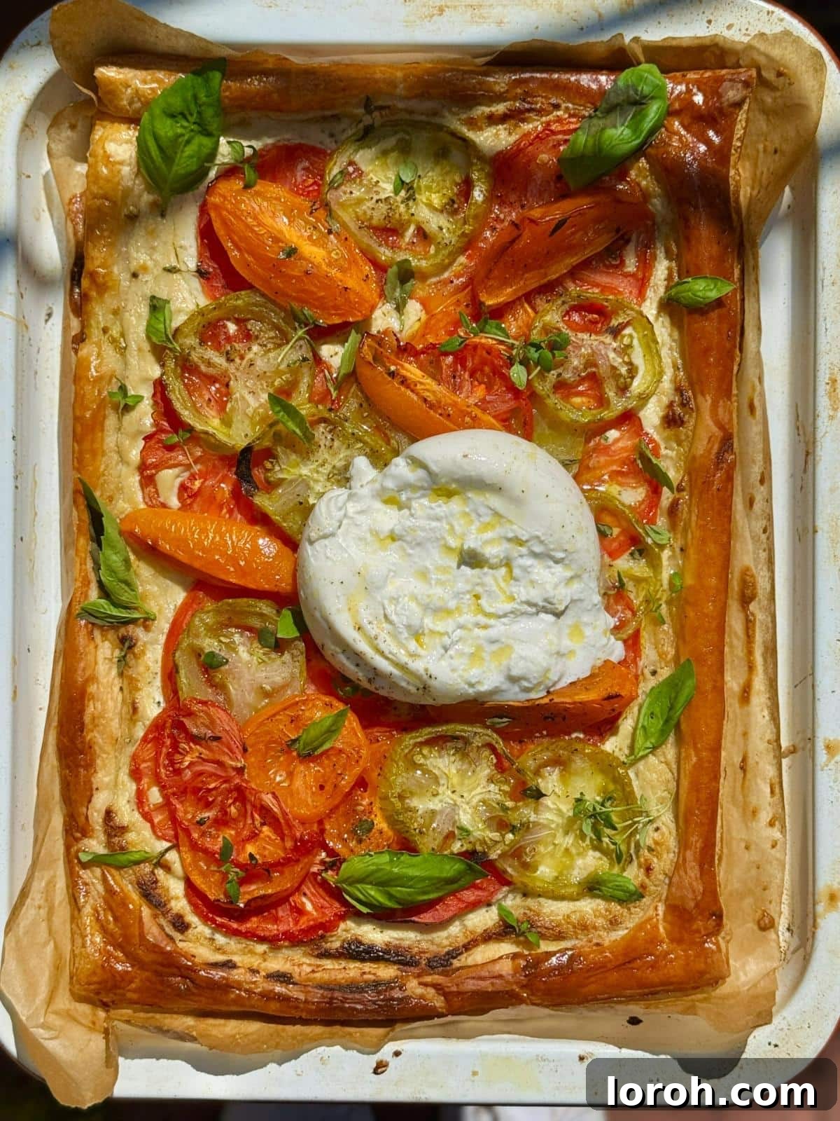 Golden tomato puff pastry tart crowned with creamy burrata and fresh basil leaves.