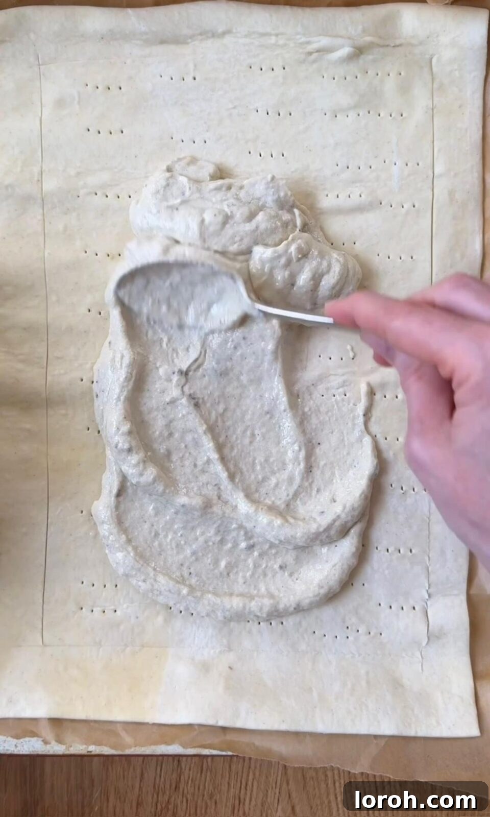 Crème fraîche mixture being smoothed over the center of the puff pastry, leaving a border.