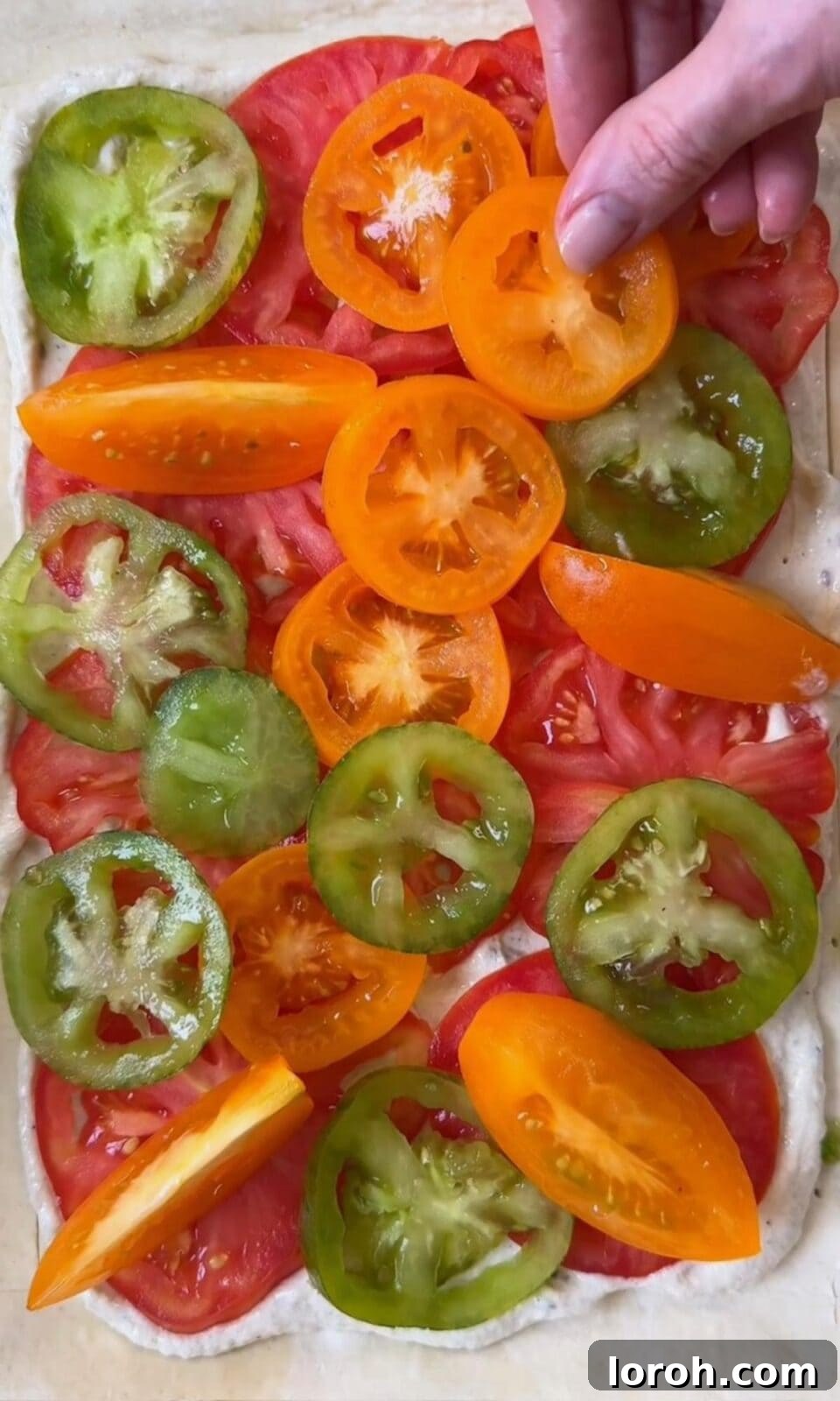 Dried tomato slices being layered artfully onto the crème fraîche-covered puff pastry tart.
