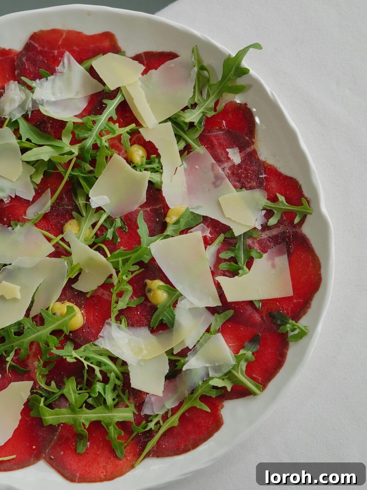 Exquisite beef carpaccio served with fresh arugula and generous shavings of Parmesan cheese, elegantly arranged.