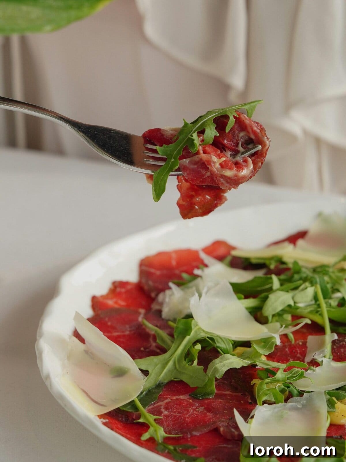 Close-up of beef carpaccio on a fork, highlighting its delicate thinness.