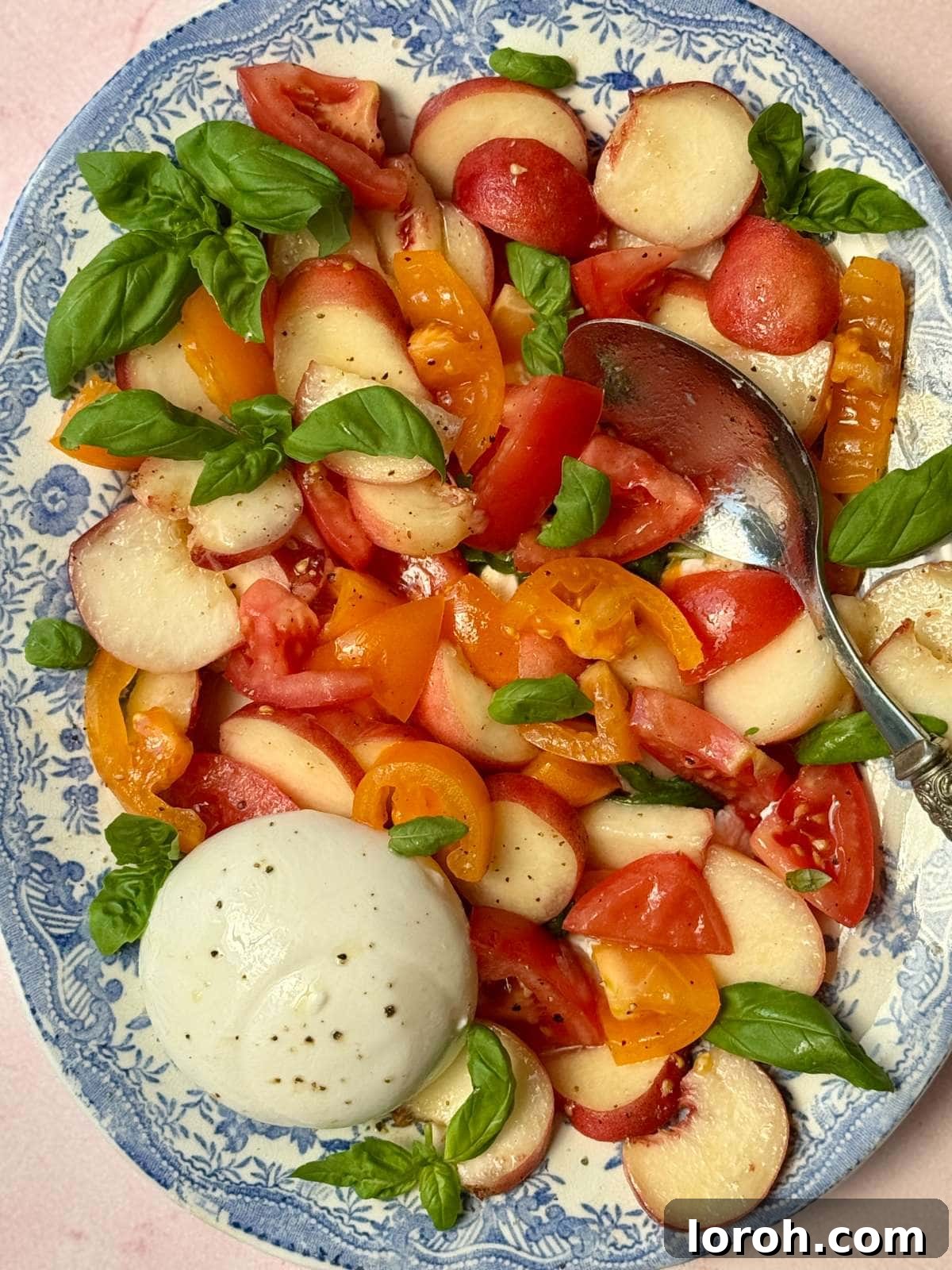 Creamy Burrata and Sweet Peach Salad 2 A vibrant burrata and peach salad elegantly arranged on a blue floral plate, showcasing fresh ingredients.