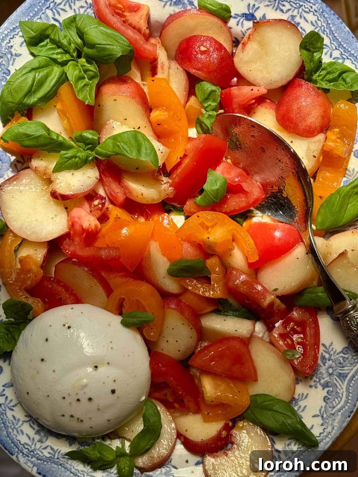 Creamy Burrata and Sweet Peach Salad 3 A close-up view of the burrata and peach salad, showcasing the creamy burrata against the vibrant peaches and tomatoes on a blue floral plate.