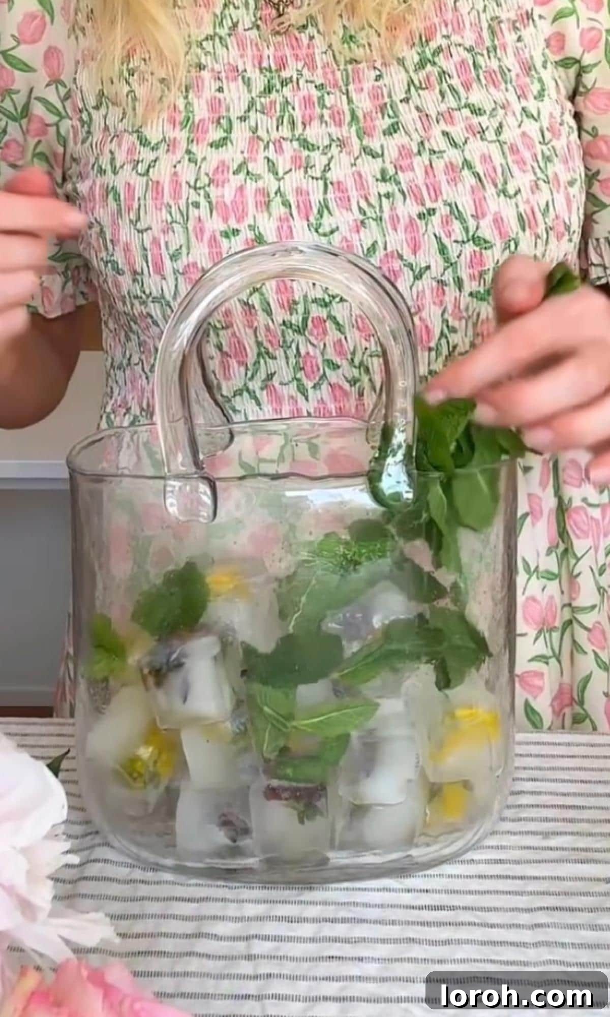 Adding ice and mint leaves to a large wine glass, preparing for a Hugo Spritz.