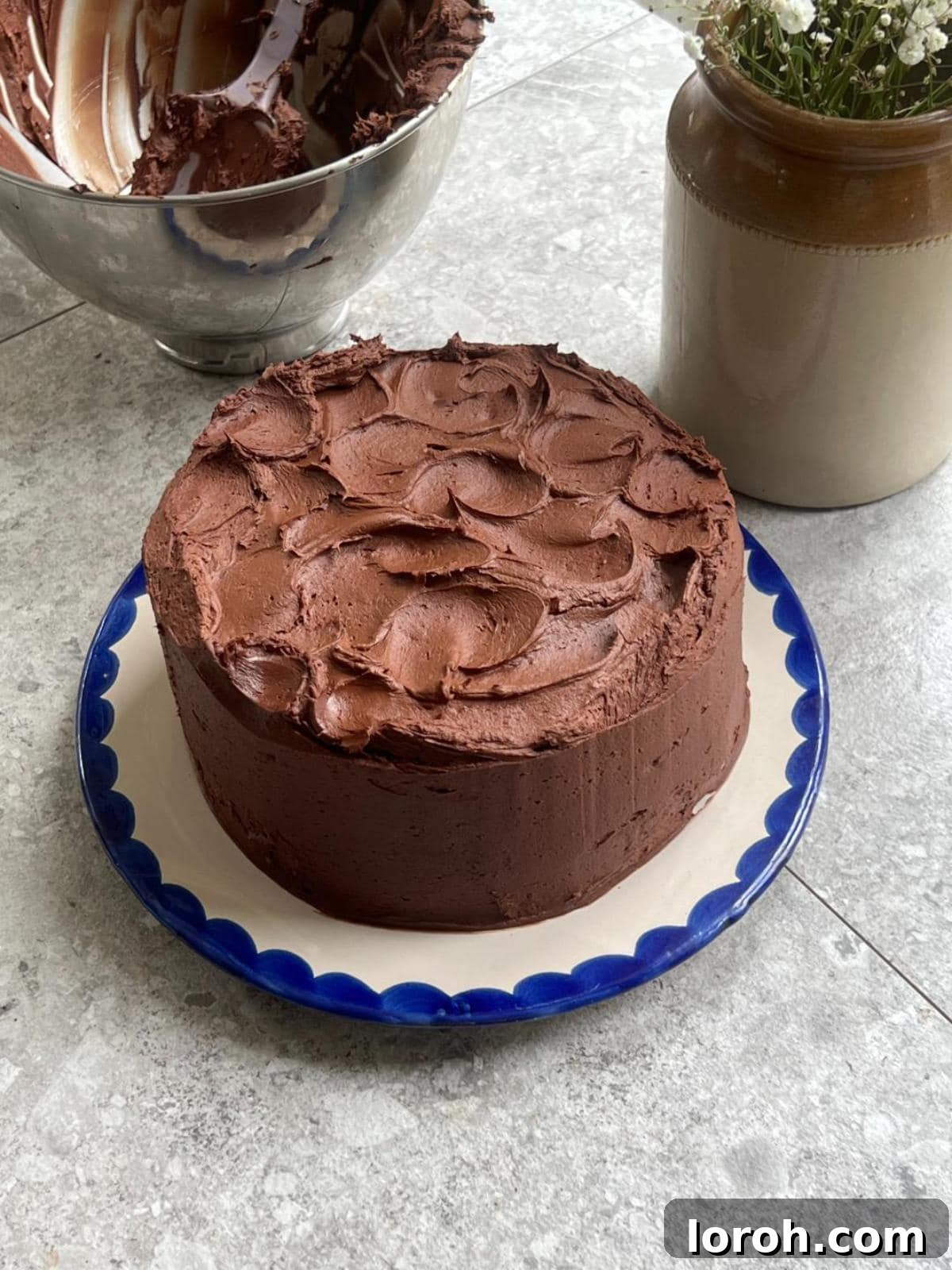 Finished Matilda's chocolate cake on a white plate with blue trim, covered in ganache.