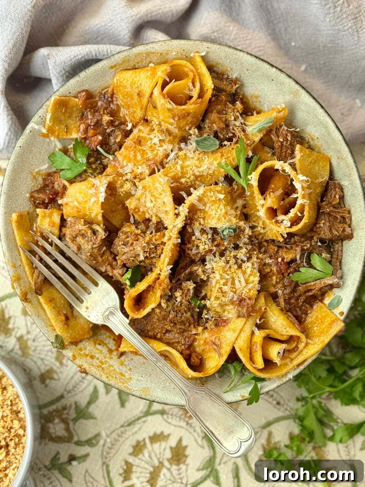 Silky Beef Short Ribs Ragu with Pappardelle Pasta, garnished with fresh herbs and Parmesan.