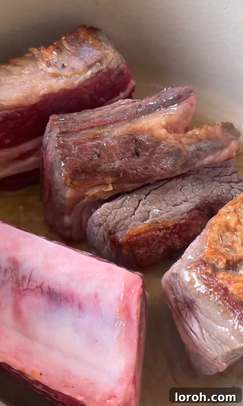 Searing bone-in beef short ribs in a Dutch oven until deeply browned.