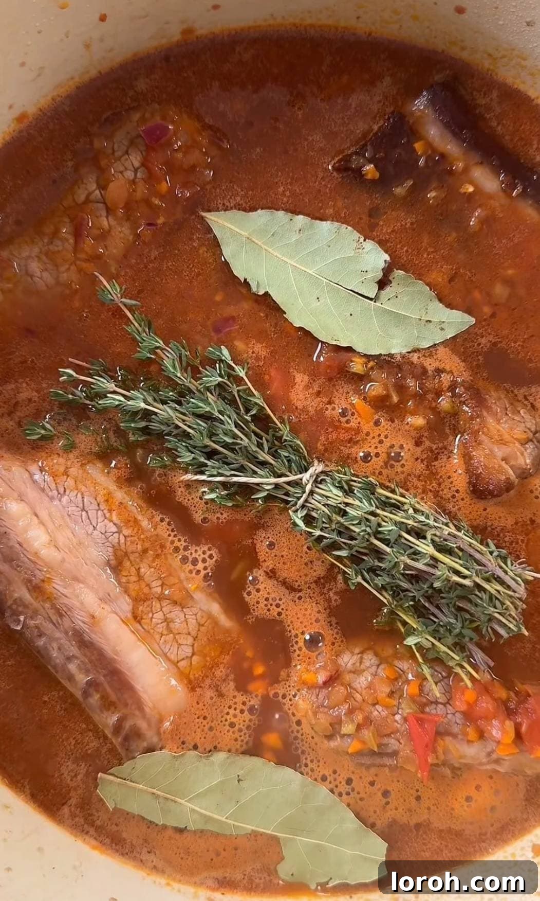 Beef short ribs ragu with thyme and bay leaves, ready for braising in the oven.