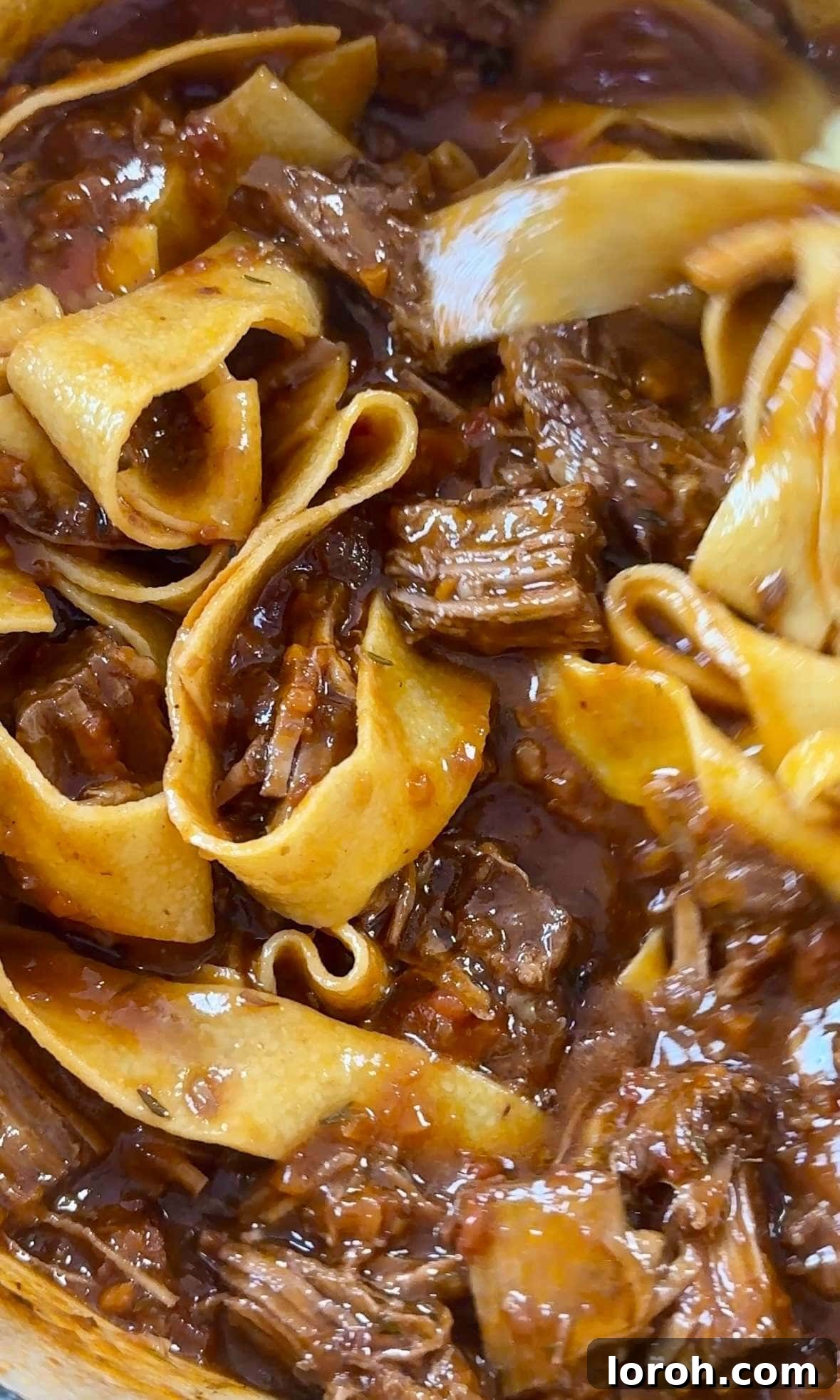 Tossing cooked pappardelle pasta with beef short ribs ragu in a large pan.