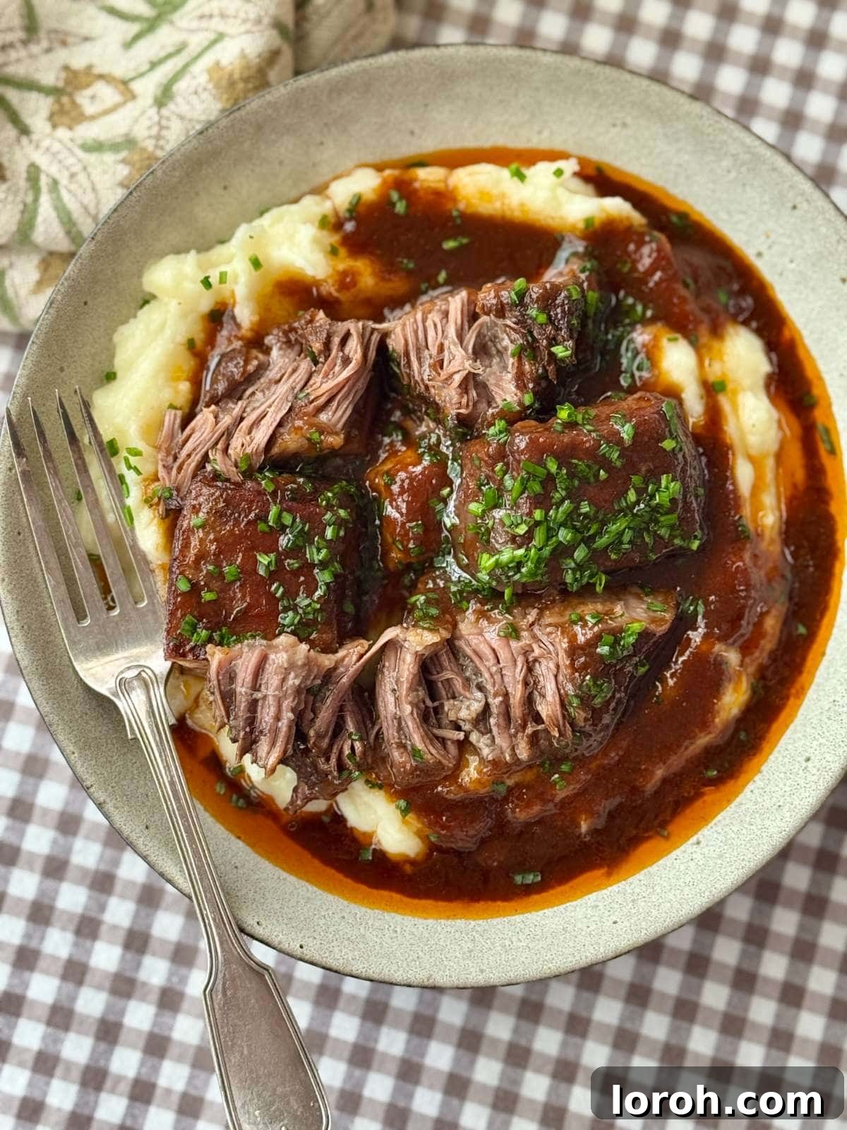 Braised beef short ribs served elegantly on a bed of creamy mashed potatoes, garnished with fresh herbs.