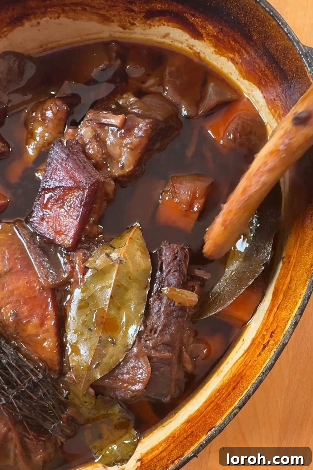 A hand gently pulling a bone clean from red wine braised beef short ribs, showcasing their incredible tenderness.