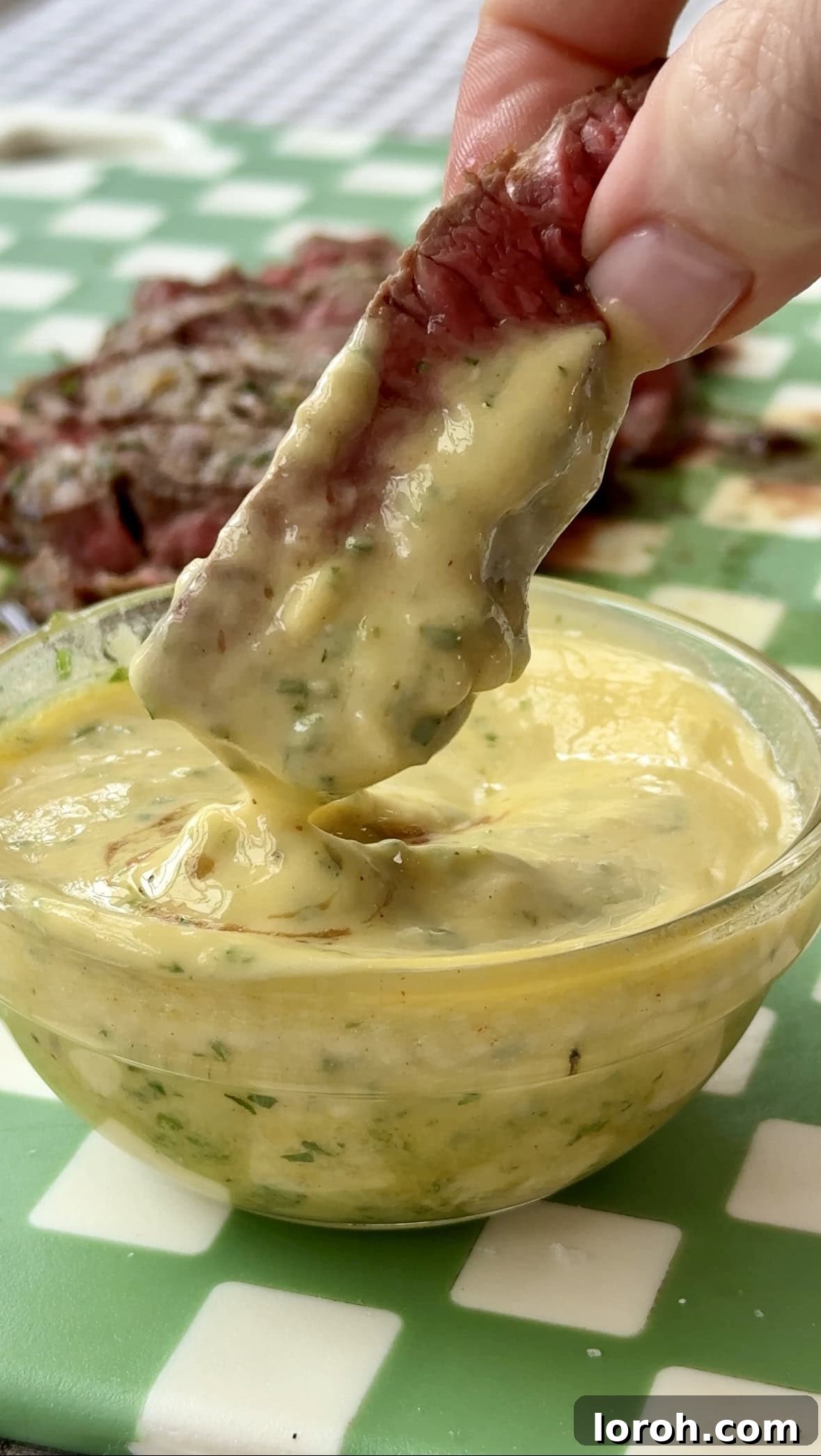 Fast Cowboy Butter Fix 2 Dipping a perfectly cooked steak into a bowl of rich, melted cowboy butter, highlighting its smooth texture and vibrant herb flecks.