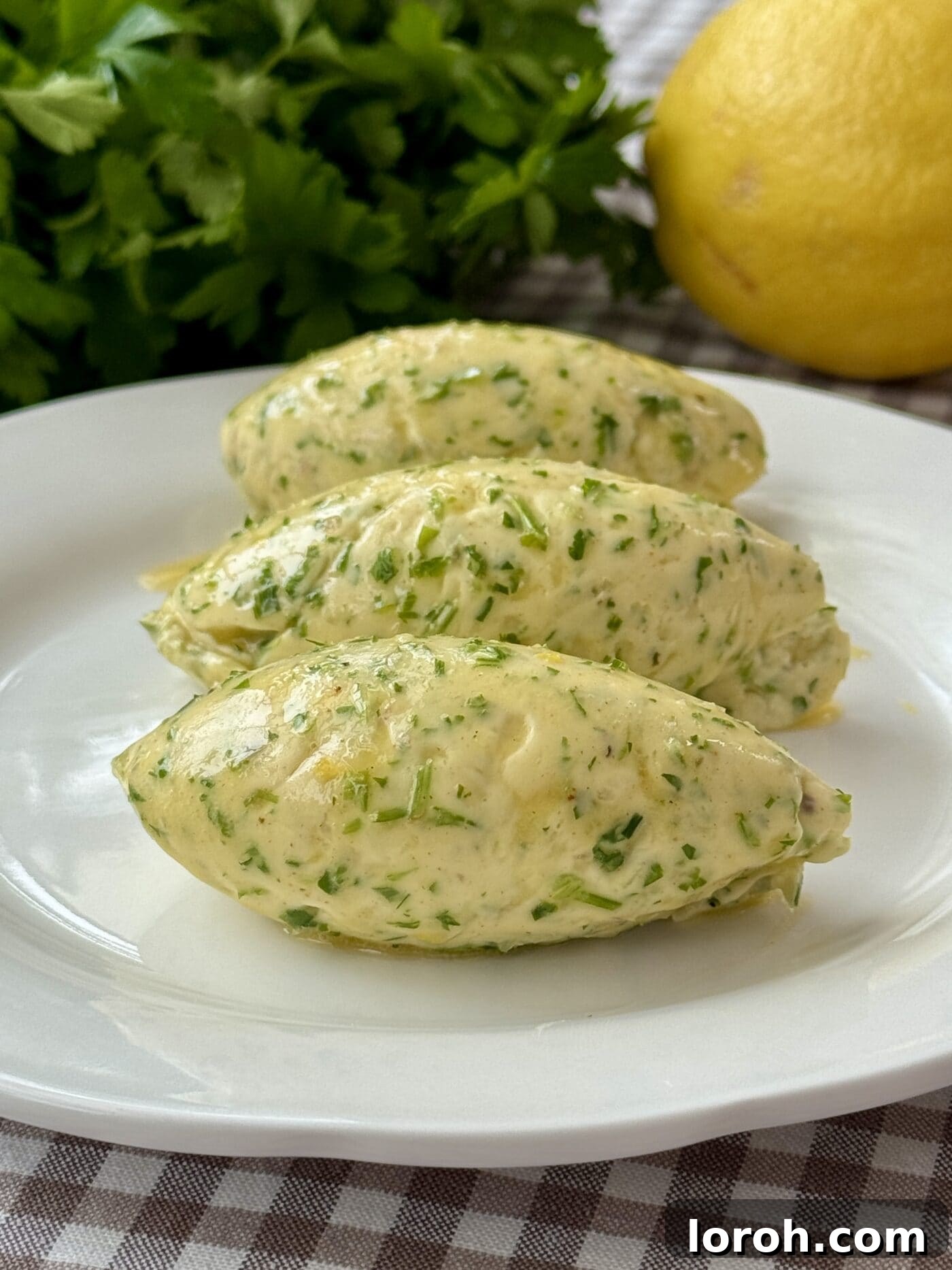 Fast Cowboy Butter Fix 3 A scoop of vibrant cowboy butter resting on a white plate, showcasing its rich yellow color and finely chopped green herbs.